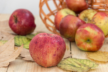 Спелые красные яблоки в деревянной корзине на деревянном фоне украшенные опавшими листьями. Здоровое питание.