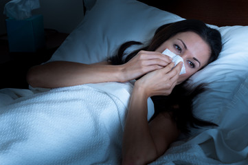 Attractive female woman sick in bed blowing nose in the Sick Woman in Bed Blowing Nose