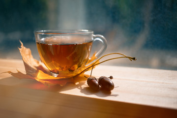 Autumn Still Life: Tea on maple leaves on a wooden table near the window. The sun's rays on a cup...