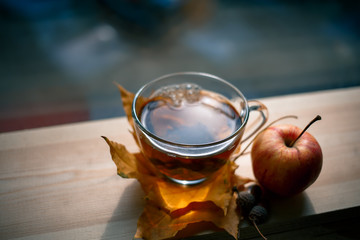Autumn Still Life: Tea on maple leaves on a wooden table near the window. The sun's rays on a cup of brewed tea. Cup of hot tea on a sunny day on a window background.