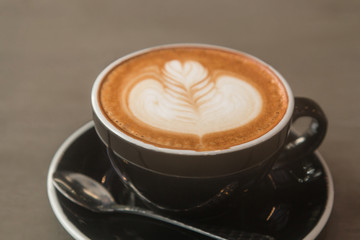 Latte hot coffee (or cappuccino) in a black cup with latte art. Gray wooden table background. Interior coffee shop. Selective focus and extremely shallow depth of field.