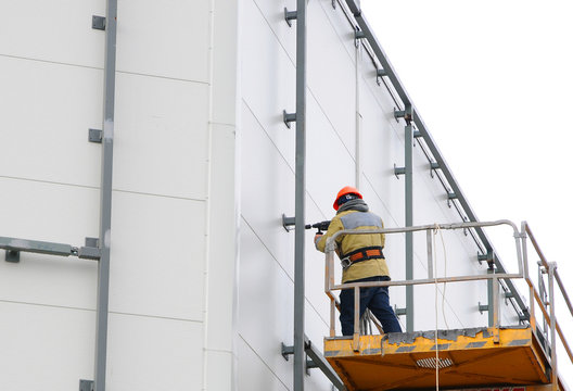 Worker in lift bucket during installation big billboard in bad weather.