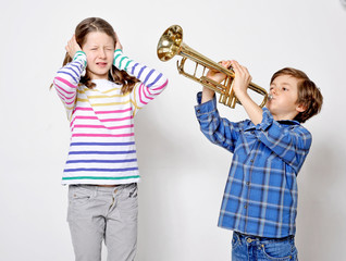 Kleiner Bruder ärgert seine Schwester mit der Trompete und provoziert sie mit Krach