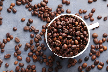 Roasted coffee beans in mug on grey table