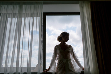 Silhouette of the beautiful bride next to the window