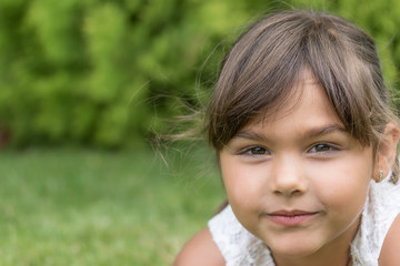 Closeup view of the slightly smiling face of little girl lying on the grass outdoors. 