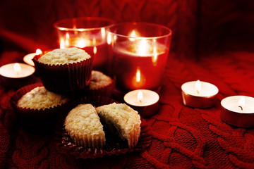 Soft focus. Muffins in a red wrapper on red knitted sweater, red candles and bokeh. Christmas atmosphere