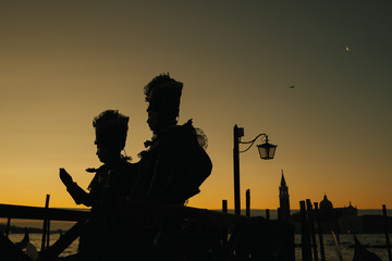 The silhouettes of a couple in carnival costumes standing in the