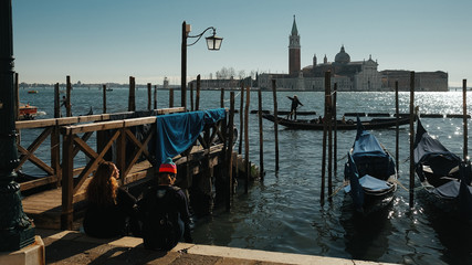 Fototapeta na wymiar Tourists sit on the berth behind the gondolas admiring Venice ci