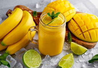 Healthy ripe Yellow Banana Mango Smoothie with slices of Lime, mint and ice
