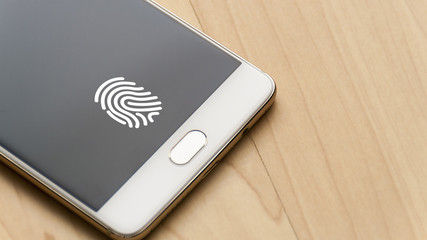 Biometric fingerprint reader on a white smartphone, with a fingerprint icon on the screen for fingerprint identification and wood background. 