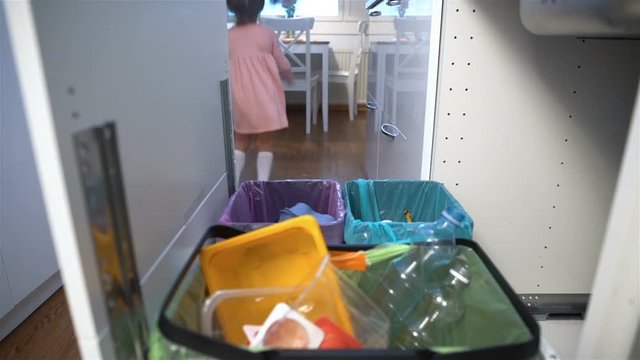 Little girl drops the trash into kitchen recycling bin.
