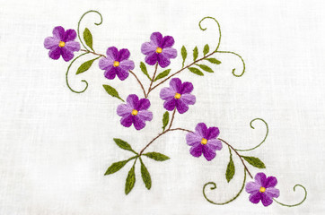 Gentle purple flowers with leaves embroidered satin stitch on white cloth