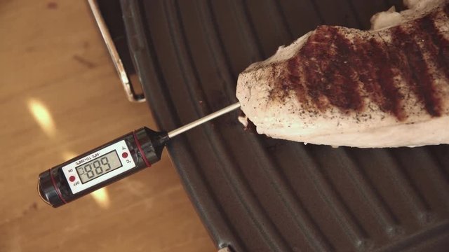 4K shot of thermometer for meat set in a large steak that is on elektrogrile shows the temperature and the degree of readiness of steak. View from above