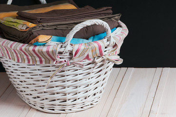 bedclothes of different colors in wicker basket on light background