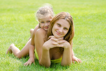 Fototapeta premium Mum and daughter lie on a green lawn in a bikini and look in the frame