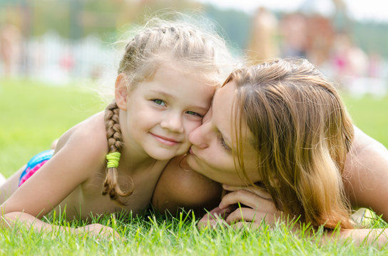 Mother kissing her daughter lying on a green grass lawn