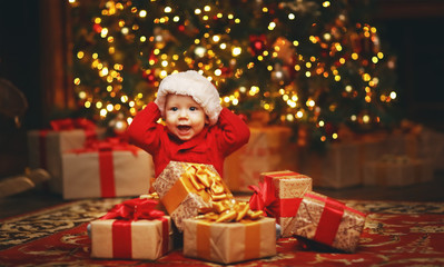 Fototapeta na wymiar Happy baby by Christmas tree with gifts