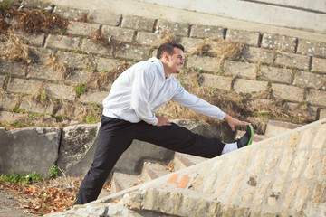 Attractive young man is exercising outdoors. He is doing stretching exercise for his legs on the staircase.