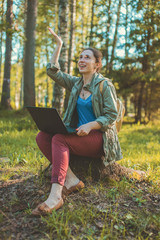 Young woman sitting in forest on a stump with computer