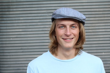 Portrait of casual blonde young man wearing glasses, news paperboy hat and blue crew neck t-shirt