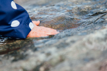 Close up detail of a baby or toddler's hand splashing a puddle on a rock with water droplets and wearing a blue polkadot raincoat