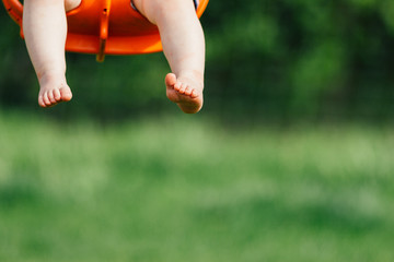 Focus on toddler girl's feet and legs as she swings in an orange baby swing at a playground