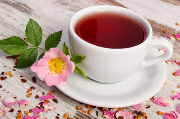 Cup of tea with wild rose flower on old rustic wooden background