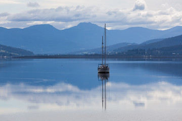 Sailboat reflecting in calm waters of Huon River. Huon Valley, Tasmania, Australia.