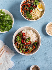 Vegetarian lunch table in the asian style - bowls with rice, noodles, vegetable stir fry. On a blue background, top view