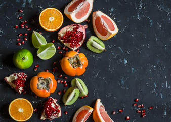 Fototapeta na wymiar Variation of fresh fruit - grapefruit, persimmon, kiwi, pomegranate, orange, lime. On the dark background, top view