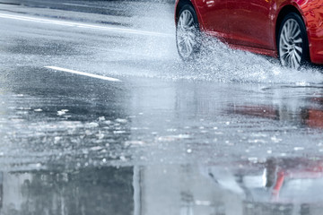 red car driving through water puddle with water splashing from its wheels
