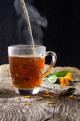 pour tea with flower petals in a cup on a wooden background