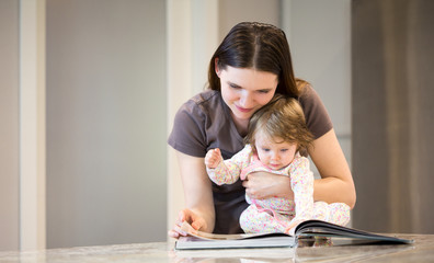 Young mother with little baby girl reading a cookbook