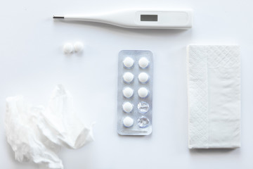 White desk with two round pills, taken from a foil case, thermometer, paper napkin and crumpled napkin on it. Top view, medicine concept photo