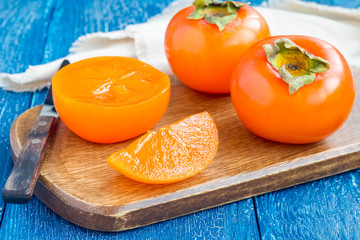 Cut persimmon fruits on wooden board and table, horizontal