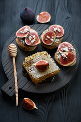 Dark wooden serving board with bruschetta made of figs and honey