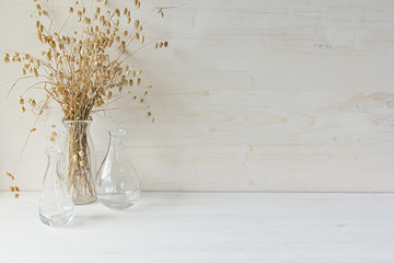 Soft home decor of  glass vase with spikelets on white wood background. Interior.