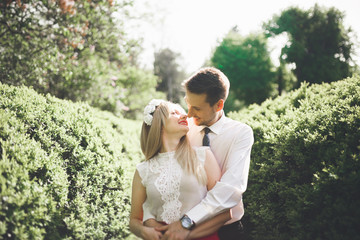 Young beautiful couple kissing and hugging near trees with blossom in summer park