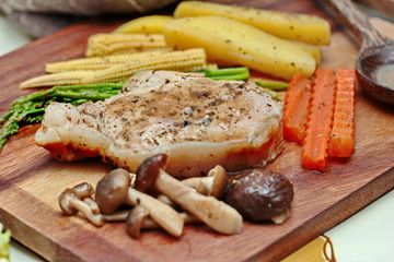 Home made,Pork steak and mixed vegetables(as sliced potato,carrot,mushroom,corn and asparagus)on butcher served with side dish as parmesan cheese bread,sausage,mushroom soup and salad.Selective focus.