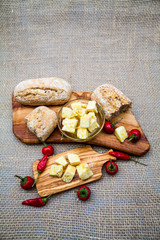 Composition with olive wood, cheese pieces in olive oil, bread and hot peppers with burlap texture in the background