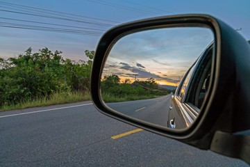  Reflection seen through car side mirror -  two-lane winding road with twilight sky and sunset

