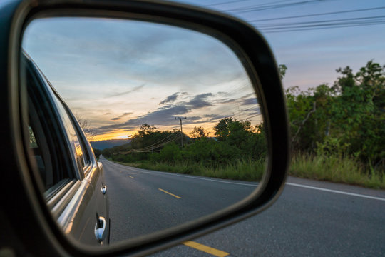  Reflection seen through car side mirror -  two-lane winding road with twilight sky and sunset
