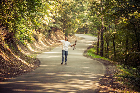 Skateboarder standing in the middle of the road in the forest and raising his hands up