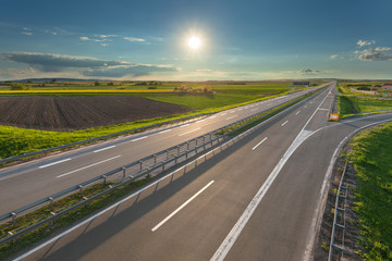 Fototapeta premium Open freeway through illuminated green agricultural fields