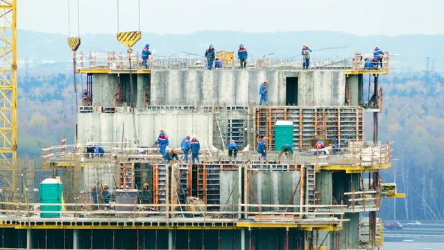 Construction workers mounting concrete formwork with crane during house building on the background of forest and road