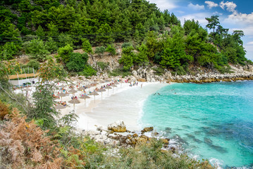 Marble beach (Saliara beach), Thassos Islands, Greece. The most beautiful white beach in Greece. Tourists enjoying a nice day at the beach. Straw umbrellas (straw parasol) and sunbeds on the beach.