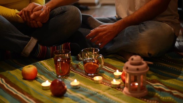 Couple on a romantic date, sitting on the floor, among a candles and  holding hands. Slow motion.