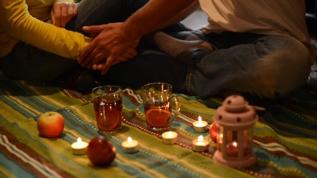 Couple on a romantic date, sitting on the floor, among a candles and holding hands.