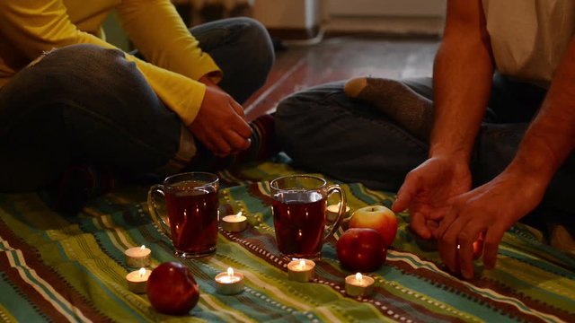 Couple on a romantic date, sitting on the floor, among a candles. Man holds in his hands a candle and handing it to the woman as a symbol of the soul. Slow motion.